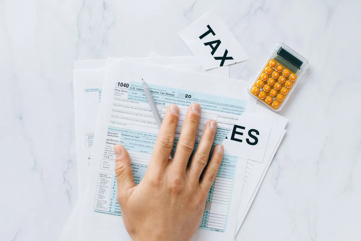 A hand filling out a 1040 tax form beside a calculator